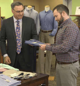 A man gets help from another man shopping for shirts. 
