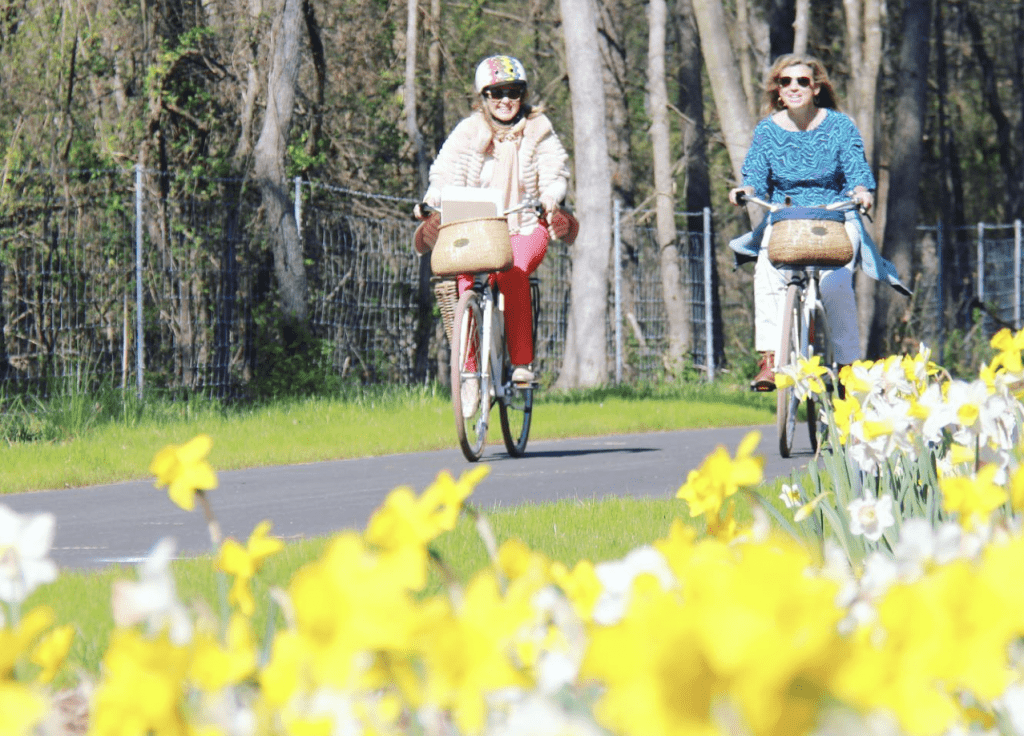Two people ride bikes along flowers with Basket & Bike