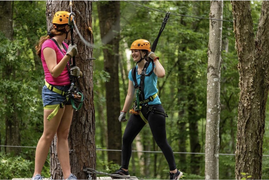 two girls on a zipline challenge course in the woods
